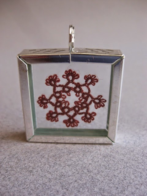 Silver frame with glass slides holding a tatted motif in silk thread