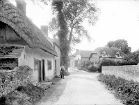 Looking up the street with the old Post Office to the left with a man holding a basket. A number of interesting verncular buildings are visible, mostly timber-framed with brick in-filling and thatched roofs. Reproduced by permission of English Heritage NMR.