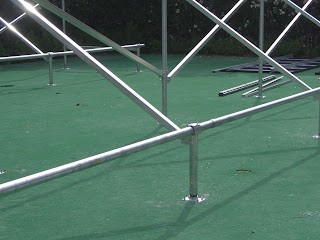 This photo shows some of the aluminum components that come with the UniRac "UL-A" kits. Front cap/brace support, slider brackets (for diagonal bracing) and the anchor plates for 3" vertical risers.  The base plates are anchored using  3/8"x3 1/2" Hilti anchors. Over to the right is a group of panels being assembled and readied for mounting.  again, due to the weight of the panels only the outer most panels were attached at this time.  This area was previously used by the owner as a putting green.  Both he and his son are avid golfers.