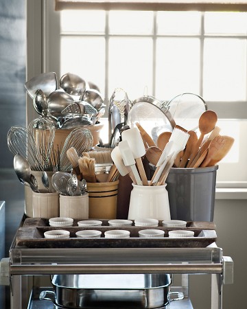 Martha keeps ladles, whisks, pastry brushes, wooden spoons, and flexible spatulas in separate containers on a cart, which is well within reach of where she is cooking.