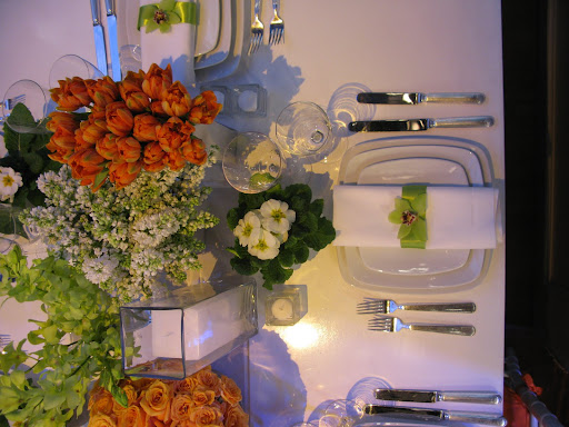 A rectangular table with several orange green and white arrangements by 