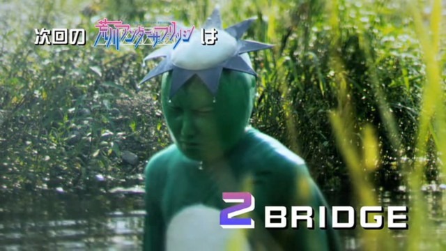 A live-action shot of a man in a kappa suit rising out of some grassy waters