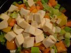 Vegetables cooking in the pan and on top, chunks of peeled, white sweet potato.