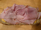 Large slices of whole-grain rye bread get some mustard, cheese, and ham.