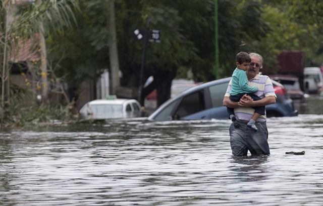 A man with a boy in his arms wades through a flooded street in La Plata, in Argentina's Buenos Aires province, Wednesday, 3 April 2013. At least 35 people were killed by flooding overnight in Argentina's Buenos Aires province, the governor said Wednesday, bringing the overall death toll from days of torrential rains to at least 41 and leaving large stretches of the provincial capital under water. Photo: Natacha Pisarenko/ Associated Press