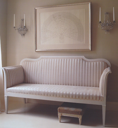 The sofa is upholstered in shades of silvery taupe and beige, and on the wall, crystal sconces and a silver frame further enhance the gleam.