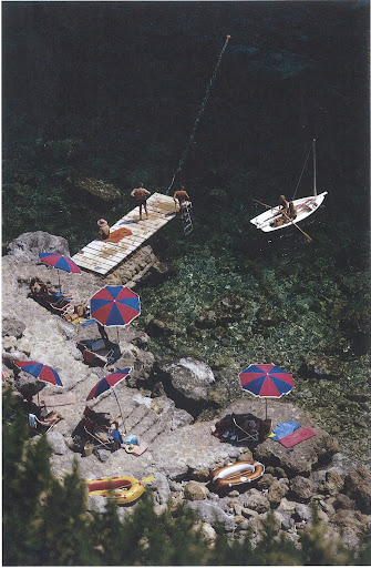 August 1973. Guests enjoy relaxing by the heated seawater pool, or lounging around the jetty by Il Pellicano's shore -- taking out a small craft or dangling their feet in the water. 'Hotel Il Pellicano