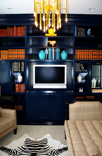 Navy blue bookcases are emboldened with sets of vintage hardback books in all ranges of oranges, browns, blues and reds. The linen furniture keeps the composition comfy. (www.domesticbliss.com)