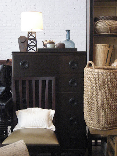 The combination of dark wood, light walls, white pillow and the rough, natural material of the woven baskets is great merchandising. The combination of dark wood, light walls, white pillow and the rough, natural material of the woven baskets is great merchandising.