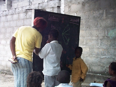 AOE14.jpg - L'institutrice apprend à ces enfants l'écriture.