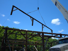 With the eave walls up and the ties in place, the first of the fifty foot long purlin plates is flown into place with its posts and braces.