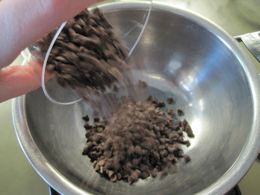 Chocolate chips are added to a bowl sitting over a pan of simmering water.