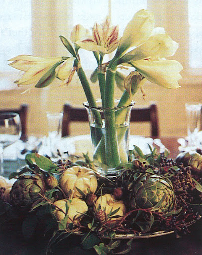 A centerpiece of amaryllis surrounded by artichokes and gourds.