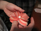 This flower is made with a stack of paper cut into the shape of an 8, with wire twisted in the middle to form a stem.  The center ball, already on a wire, gets twisted on and then petals get fanned out.