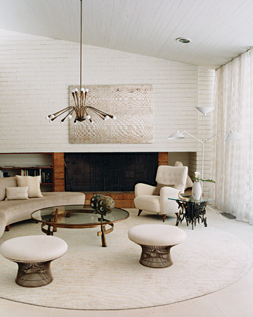 This living room features circular shapes, including a sofa by Modernica, Warren Platner stools, and a chandelier by Gaetano Scolari, all in a snowy-white hue.