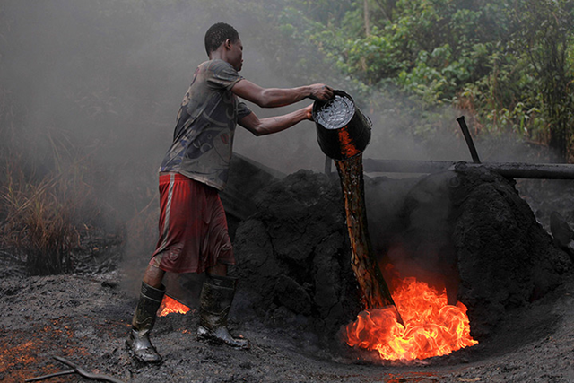 A labourer feeds a fire with crude oil at the illegal refinery. The Nigerian government's military crackdown against the theft of crude in the Niger River delta has left more than a 1,000 makeshift refineries in flames, worsening pollution in the area Photo: Akintunde Akinleye / Reuters