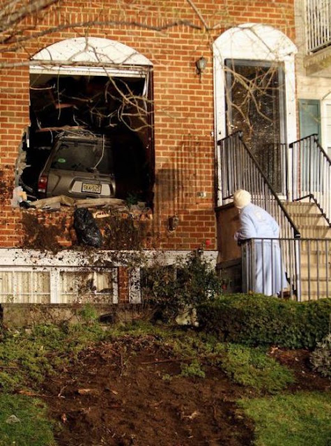 A neighbor takes a peek at a Nissan Pathfinder which crashed and landed in the house belonging to Gloria Sinclair, 74, Friday night December 8, 2011, near the intersection of West Market Street and Wickliffe Street in Newark. No one was injured, but Ms. Sinclair was home at the time with her daughter and 2 year-old grandson. A few short minutes before the accident, her grandson had left that room, a computer room, which the suv crashed into.  Saed Hindash/The Star-Ledger