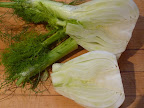 Half fennel bulb in front with stalks and fronds removed.
