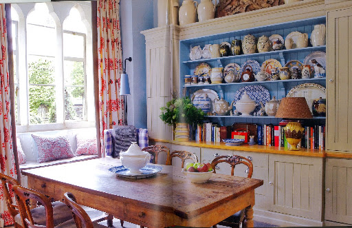 William Yeoward's country home kitchen features a window seat, piled with cushions, plus a rustic oak table.