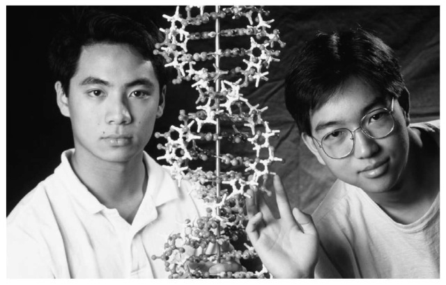 Two high school students pose with a model of a DNA molecule. 