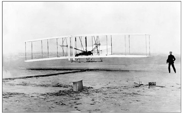 The Wright Flyer, with Orville Wright at the controls and Wilbur Wright looking on, makes its first flight, 120feet in distance, on December 17, 1903.