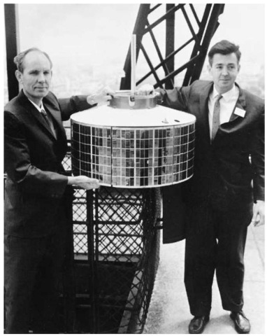 Hughes engineers Dr. Harold Rosen (right) and Thomas Hudspeth hold a prototype of the geosynchronous Syncom satellite atop the Eiffel Tower during the 1962 Paris Air Show.