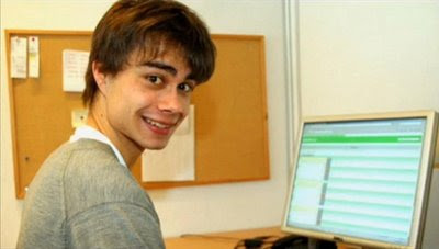image shows Alexander Rybak sitting at a laptop, side profile with big smile and eyebrows to the camera