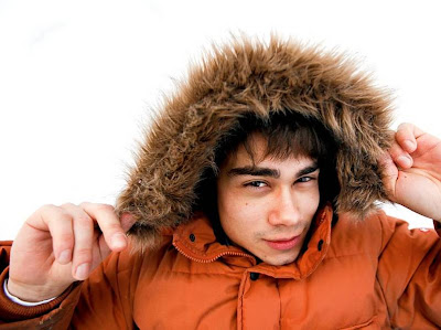 image shows Alexander Rybak smiling at the camera, wearing a big eskimo style hood on a bright orange coat