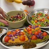 Close up of rainbow salads, homemade raw bread topped with seed/veggie pate and more veggies. Plus a tiny falafel patty in the front.