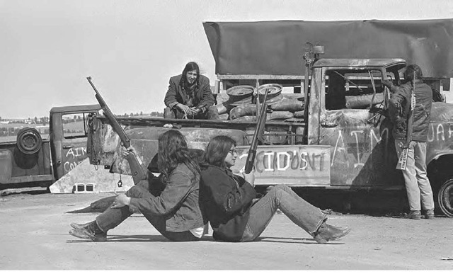 Wounded Knee, South Dakota. Armed Indians sit back to back supporting one another and watching in all directions as members and supporters of the American Indian Movement (AIM) hold this small village. 