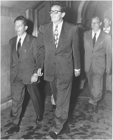 Hollywood screenwriter Ring Lardner, Jr., being led away in handcuffs to serve a one-year jail sentence for refusing to answer questions before the House Un-American Activities Committee. Lester Cole and Herbert Biberman in background. 