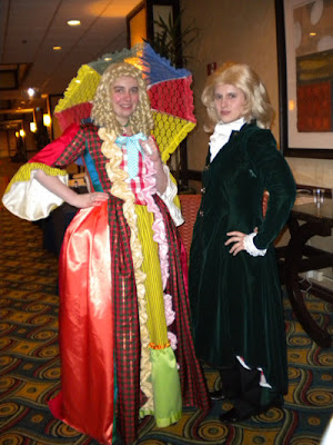 The female Sixth Doctor cosplayer described above faces the camera. To her left is a woman wearing a deep green velvet surcoat over a ruffled blouse: a variant Third Doctor costume.