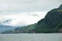 The slope of a hill all the way to the water level next to lake Lucerne, with another fog covered hill in the background - Thumbnail