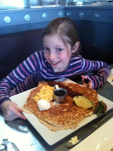 a girl sitting at a table with a plate of pancakes