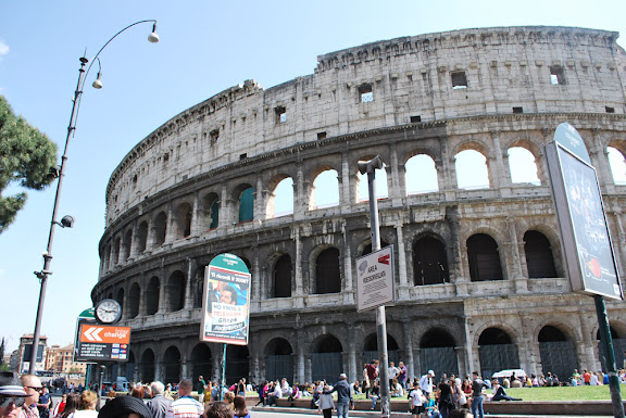 a large circular building with many arches with Colosseum in the background