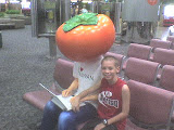 Zachary at CKS Airport sitting by a bit tomato head advertisement