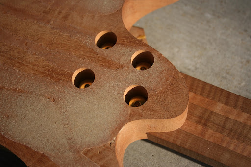 Neck heel with the bolts deeply recessed. They're drilled out to 1/2" thickness on the neck heel and 1/2" thickness on the neck. Because the neck is being held by the threads on the bolts and the steel inserts, there's no concern over threads tearing out of the wood. The neck is being held on with more compression force than you'd likely be able to get with screws in wood alone.