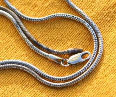 Sterling silver chain. Half cleaned of tarnish. Half tarnished. Snake chain. Half was submerged in cleaning solution, half was left hanging out of pan to remain tarnished