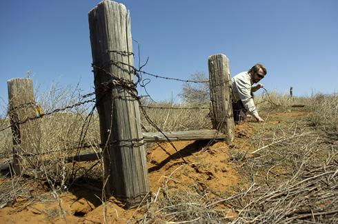 Wildlife Refuge Manager Jude Smith explains how a fence post has been buried by tumbleweeds and soil over time at the Muleshoe National Wildlife Refuge, near Muleshoe, Texas. Smith believes a couple fences are buried beneath this fence. By Geoffrey McAllister, for USA TODAY