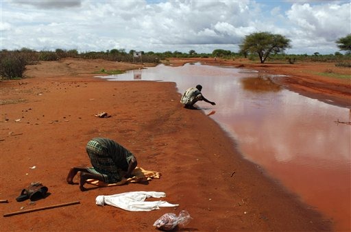 This 22 Oct 2009 photo shows a Somali Kenyan man praying as another washes his hands in flood waters after a rain storm in the settlement of Dela in N. Kenya near the Somali border. The traditional way of life for Kenya's 3 million nomads is rapidly giving way under the pressures of increasingly severe and frequent droughts, and a rapidly rising population. In one particularly drought-prone district in Kenya, up to a third have had to settle permanently because they have lost so many animals. Karel Prinsloo