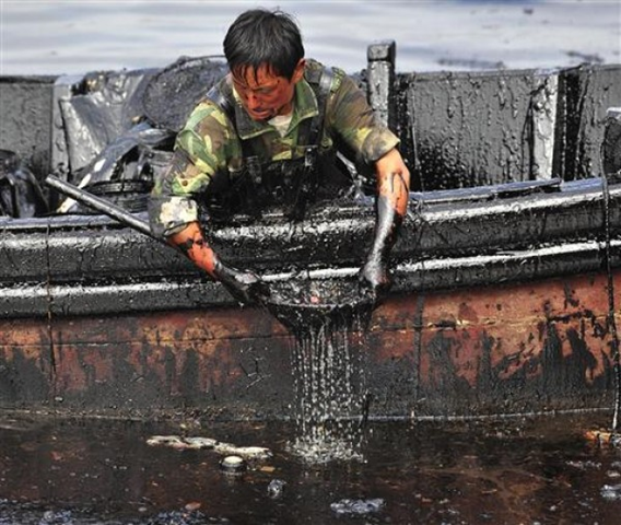 A worker scoops spilled oil from the water at Dalian's Port in China's Liaoning province, posted July 29, 2010. REUTERS