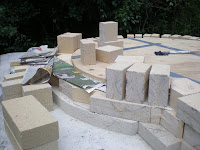 The plywood protects the floor bricks from dropped mortar.  The newspaper keeps the first (soldier) course from bonding to the floor.