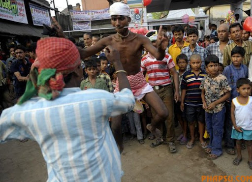 Onlookers watch as Indian Hindu devotees (foreground) dance with their tongues pierced with metal rods during the ritual of Shiva Gajan at a village in Bainan, some 80 kms south of Kolkata, on April 14, 2010. Devotees believe that by enduring the pain, Shiva, the Hindu god of destruction, will grant their prayers. Thousands took part in the month-long festival which culminates with the worship of Shiva on the auspicious day of Chaitra Sankranti, the last day of the Bengali calendar year.    AFP PHOTO/Deshakalyan CHOWDHURY (Photo credit should read DESHAKALYAN CHOWDHURY/AFP/Getty Images)