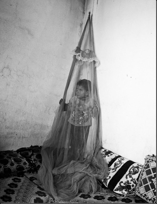 Khoder, 10, stands behind a mosquito net inside a temporary house in the Bekaa Valley, Lebanon. (Moises Saman/Magnum Photos for Save the Children)