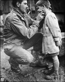American soldier Walton Trohon cleaning the face of a young French orphan, France, 25 November 1944