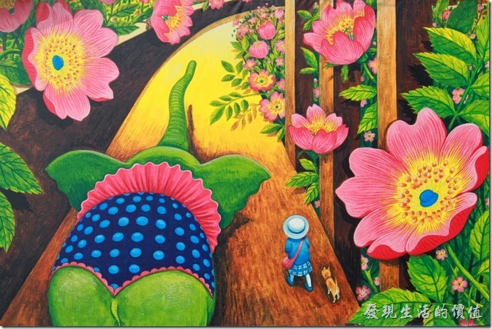 台南-土溝村(幾米)。在「幾米」塑像身後的牆壁上有一幅幾米色彩鮮艷的畫作，大象、小狗陪著小女孩走在充滿巨型花朵的道路上。