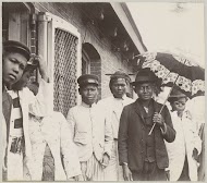 Mannen en vrouwen voor een huisje, vermoedelijk op een haventerrein