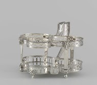 Houder van olie- en azijnstel bestaande uit twee glazen flessen en een peperbus van zilver.