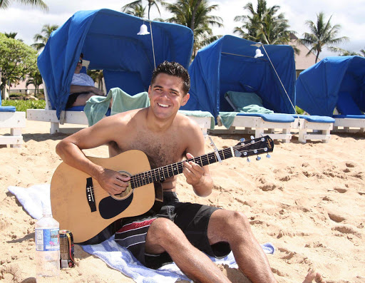 A young man entertains passers-by on guitar on Maui's Kaanapali Beach, rated one of the best beaches in the world by Condé Nast Traveler and other travel publications.  