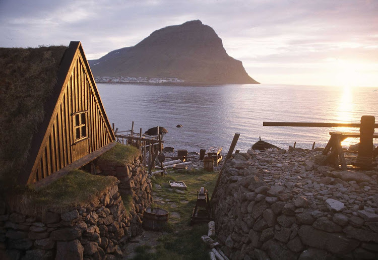 A traditional turf house by the sea at sunset in Iceland.